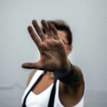 Close-up of a person's hand raised in a stop gesture, against a neutral background.