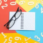 Colorful flat lay with notebook, eyeglasses, and scattered numbers on vibrant background.